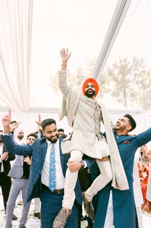 Groom lifted by guests during a lively Baraat procession, showcasing vibrant energy in South Asian Wedding Traditions.