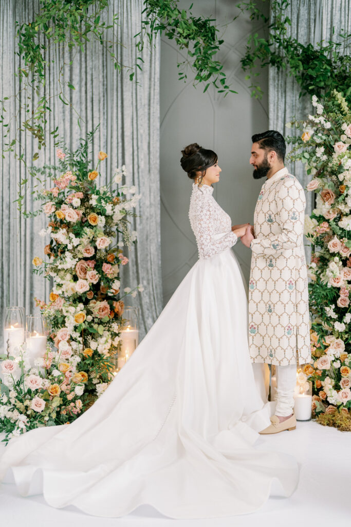 Luxury wedding couple standing under floral arch with soft neutral decor and romantic candlelight