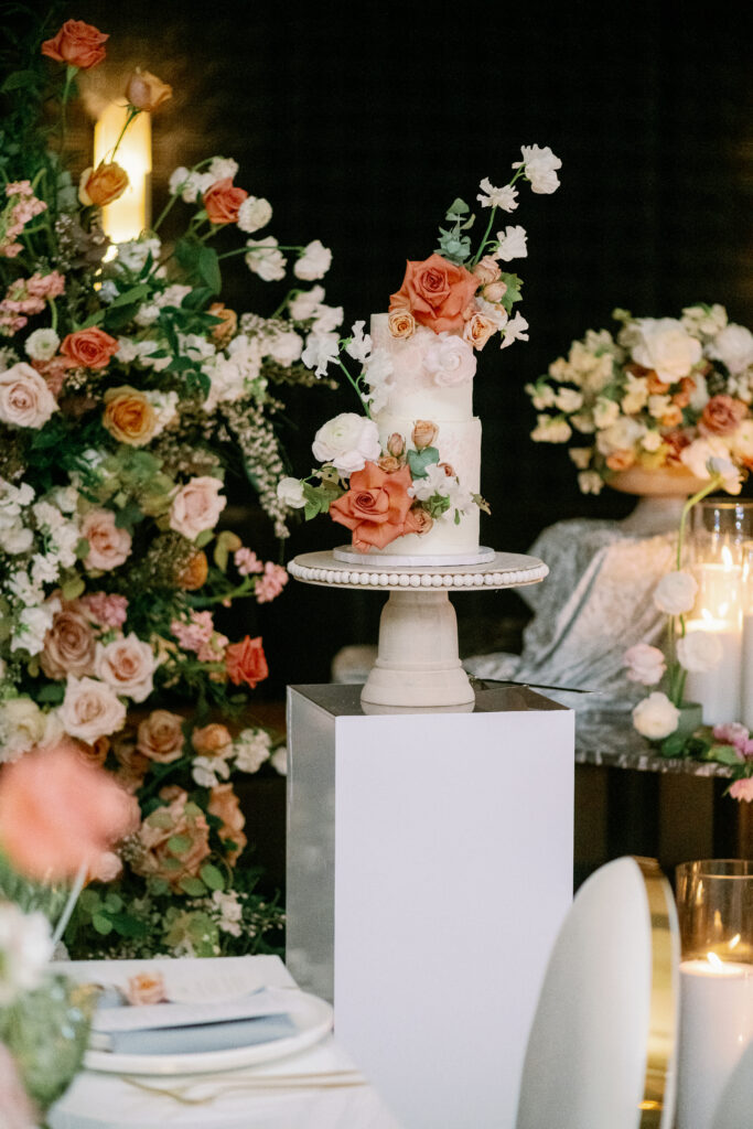 Elegant wedding cake with floral details displayed on pedestal with romantic candle and flower decor