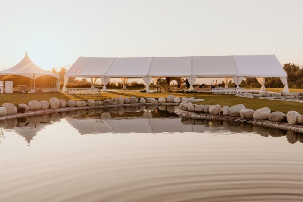 Outdoor wedding tent setup by the water at sunset with soft draping and open layout, reflecting elegant South Asian wedding decor for a destination celebration