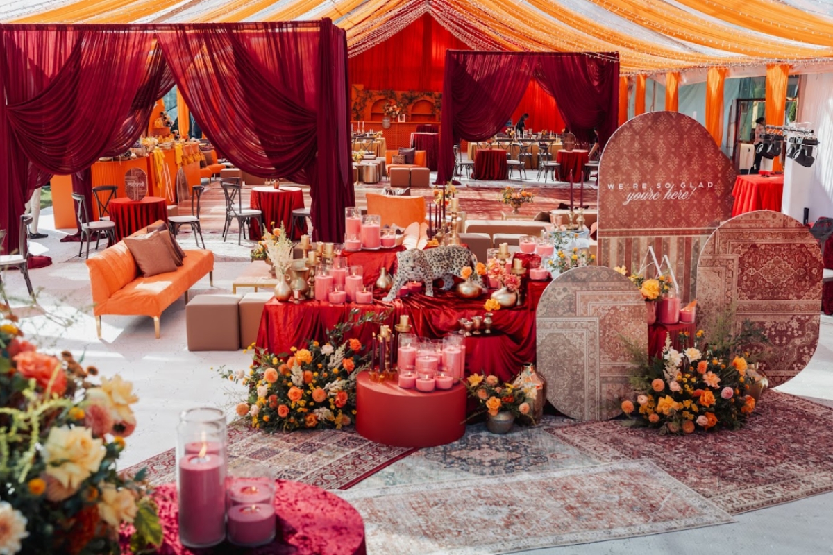 Vibrant red and orange lounge setup with layered textiles, candles, and florals showcasing bold South Asian wedding decor and reception styling