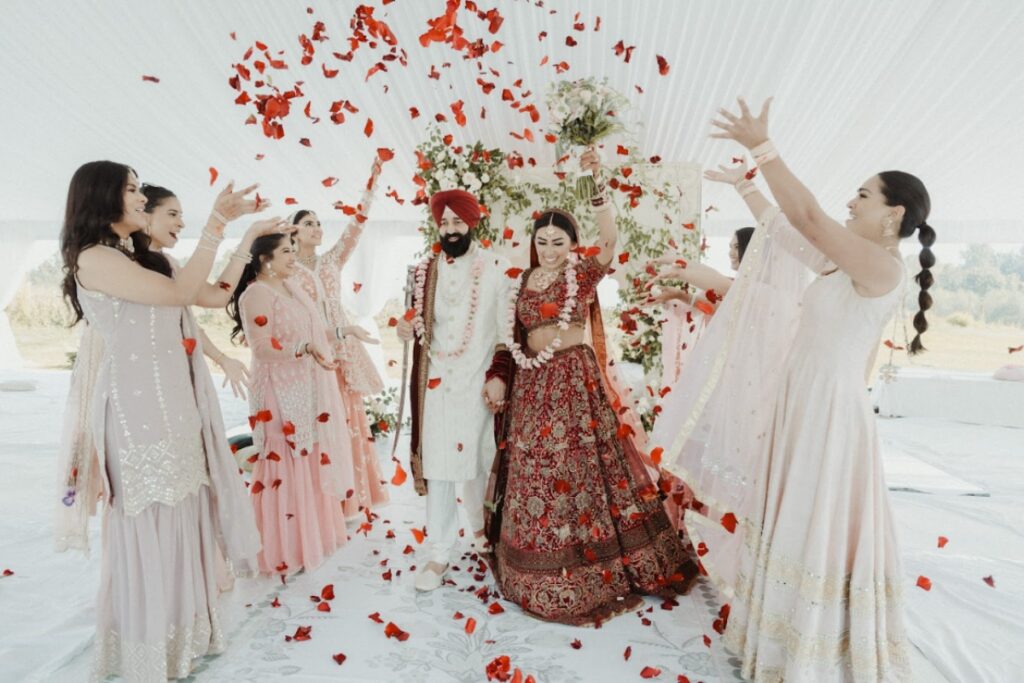 Sikh wedding planner coordinating a joyful ceremony moment as bride and groom walk through rose petals surrounded by guests