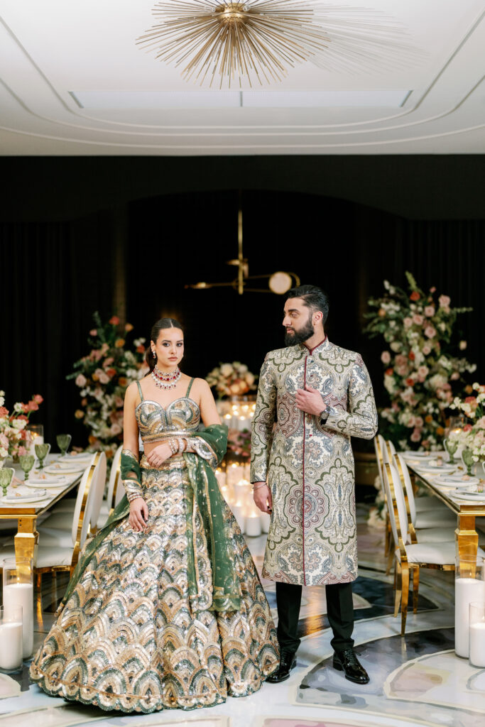 Elegant couple in traditional attire standing in a candlelit reception space with floral arrangements and refined South Asian wedding decor