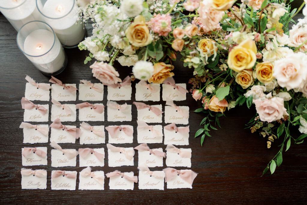 Escort card table with handwritten place cards, silk ribbons, and florals styled as part of South Asian wedding decor